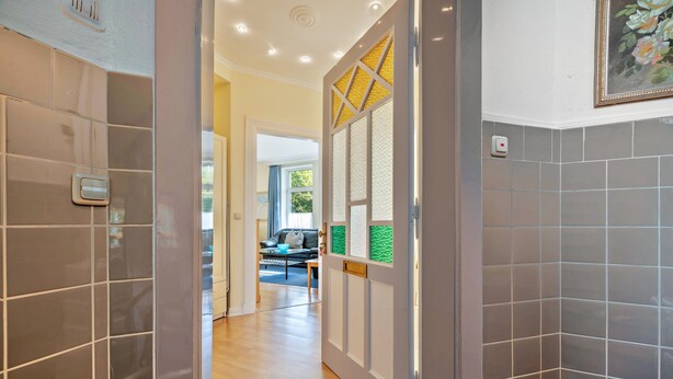 A hallway with grey tiled walls, a wooden floor, and a door leading to a living area with a sofa and a coffee table. - Apartment '4' with Wi-Fi (Cuxhaven)