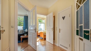 A hallway with wooden flooring, white doors, and a view into a room with a bed, window, and a blue curtain. - Apartment '4' with Wi-Fi (Cuxhaven)