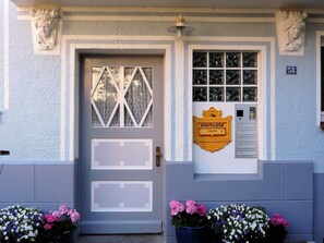 A building facade with a door, a window with a geometric pattern, a mailbox, and flower pots.