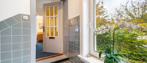 A bathroom with a shower, a window with a view of trees, and a potted plant on the windowsill.