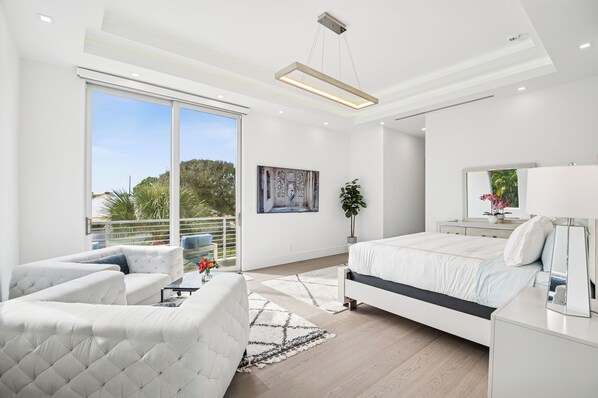 A modern bedroom with a large bed, a sofa, and a balcony with a view.
