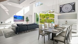 A modern kitchen with a dining area, a large window with a view of greenery, and a ceiling with skylights. - Luxury New Modern Beach Mansion in BEST Location! (Jupiter)