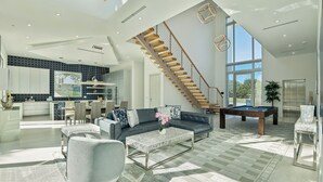 A spacious living area with a modern staircase, a pool table, and a comfortable seating arrangement. - Luxury New Modern Beach Mansion in BEST Location! (Jupiter)