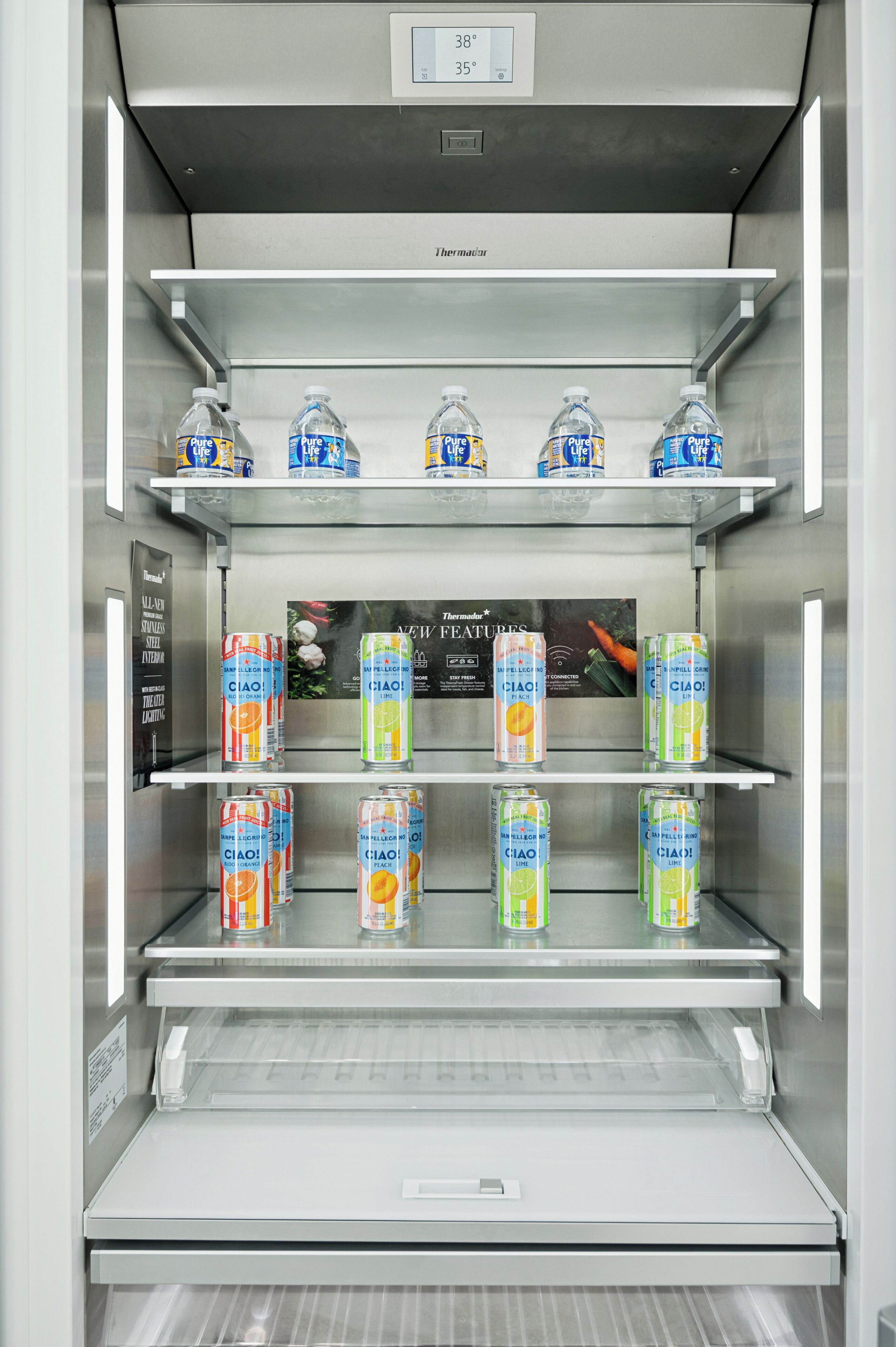 A stainless steel refrigerator with shelves stocked with bottled water and canned beverages.
