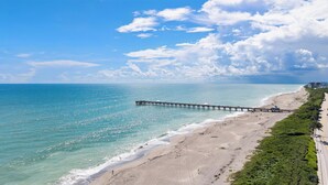 A beach with a pier extending into the ocean, a clear sky, and a road alongside the beach. - Luxury New Modern Beach Mansion in BEST Location! (Jupiter)
