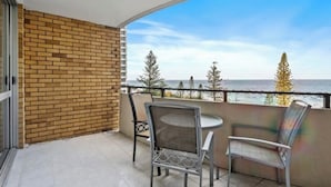 A balcony with a brick wall, two wicker chairs, and a table. - The Sands Beachfront city centre (Surfers Paradise)