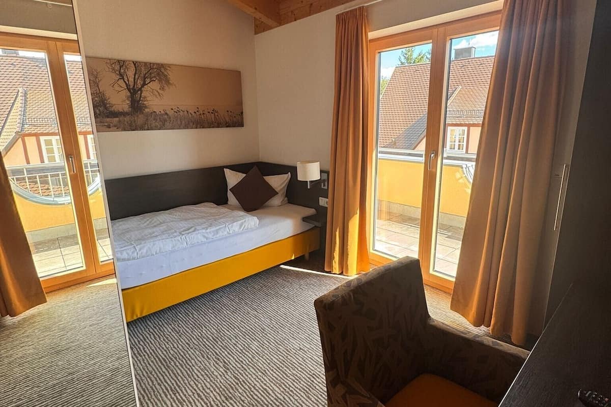Ein Hotelzimmer mit einem Bett, einem Sessel, einem Bild an der Wand und einem Fenster mit Vorhängen.