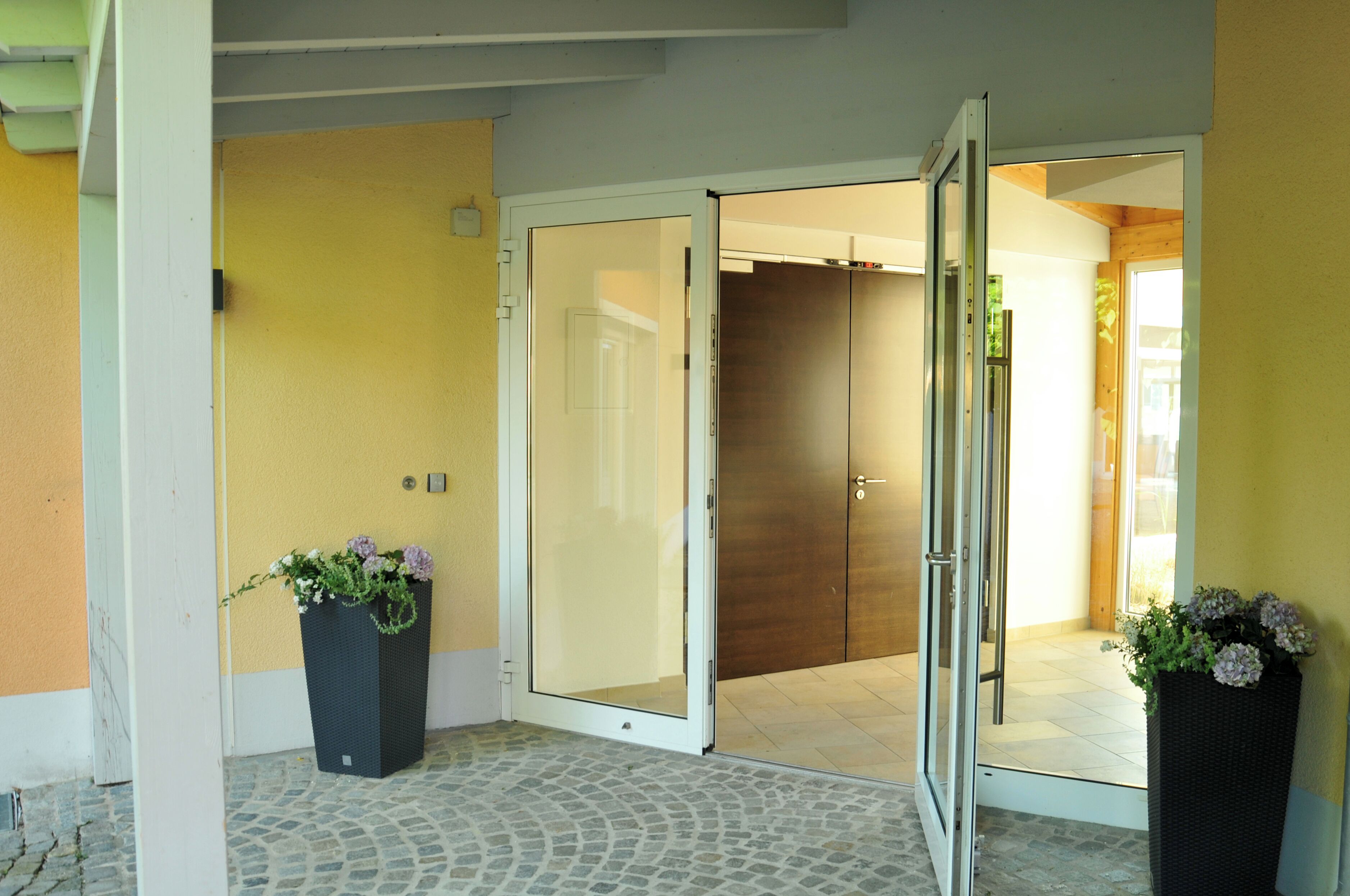 Entrada de un hotel con puerta de vidrio, una planta en maceta y piso de baldosas.