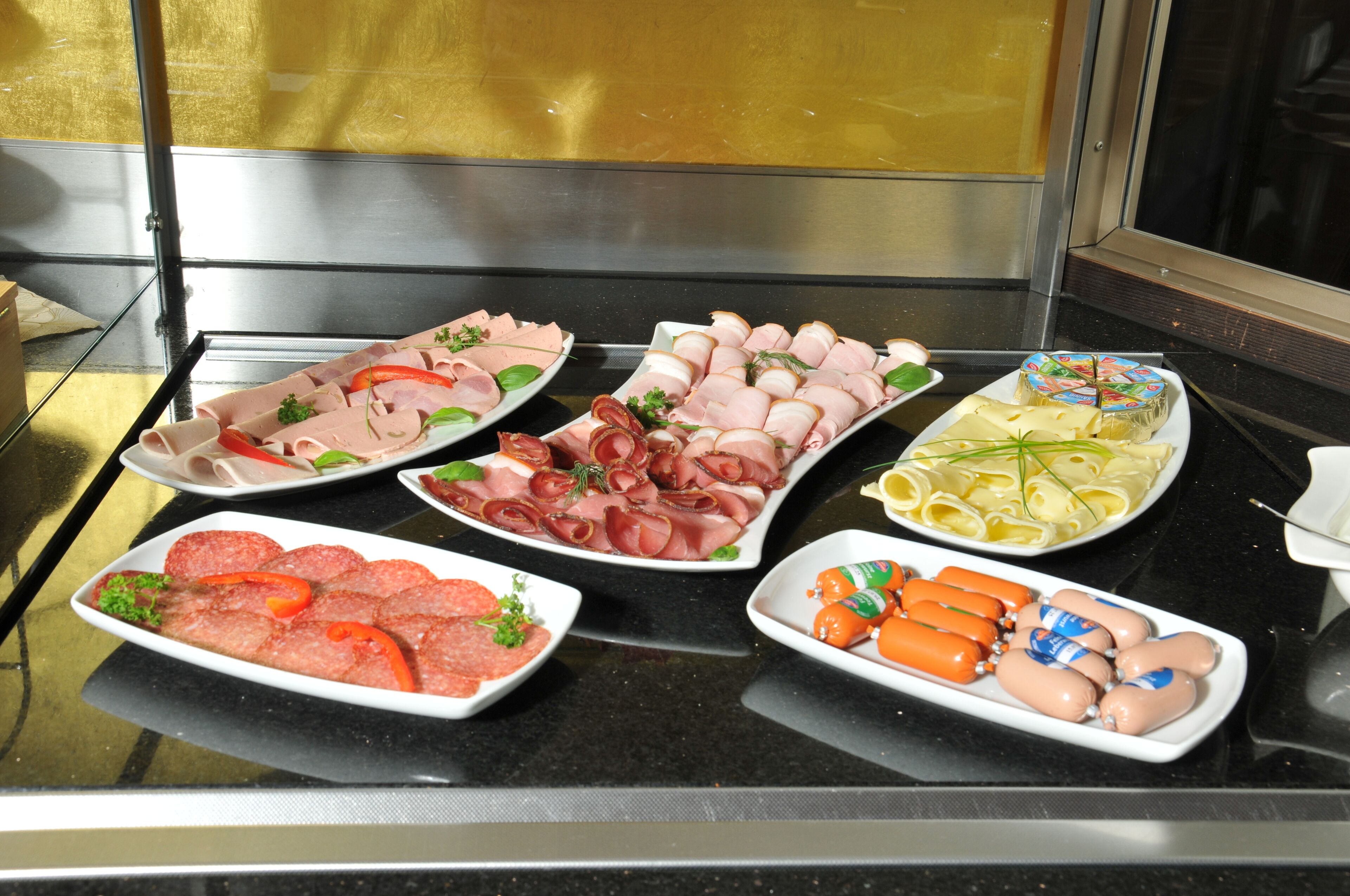 A buffet with various types of sliced meats, including ham, salami, and sausages, arranged on white plates.
