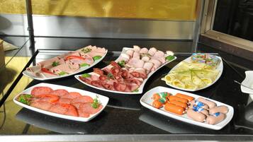 A buffet with various types of sliced meats, including ham, salami, and sausages, arranged on white plates.