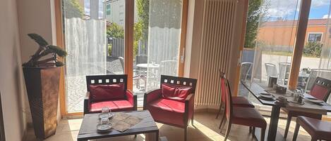 Una habitación soleada con vigas de madera, un divisor corredizo de vidrio que da al exterior, muebles rojos y una planta en maceta.