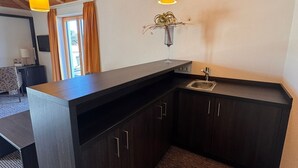 Une cuisine moderne avec des meubles en bois foncé, un plan de travail noir et un petit évier. Deux suspensions sont fixées au plafond au-dessus de l’évier.
