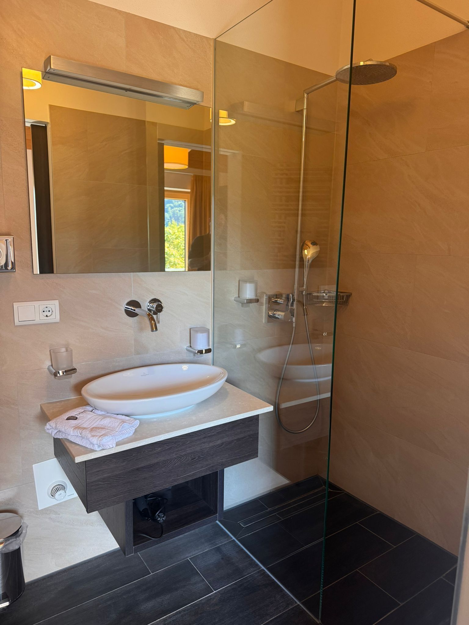 Een moderne badkamer met een douchecabine van glas, een groot ovaal wastafel en een badmeubel van donker hout.