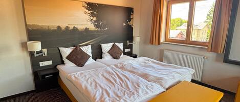 A bedroom with a large bed, a bedside table, a bench, a window with curtains, and a painting on the wall.