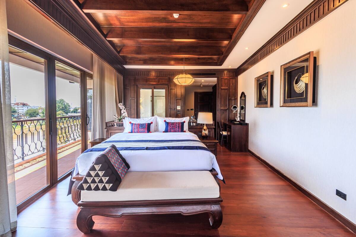 Une chambre spacieuse avec un grand lit, un plancher en bois et un balcon doté d’une balustrade.