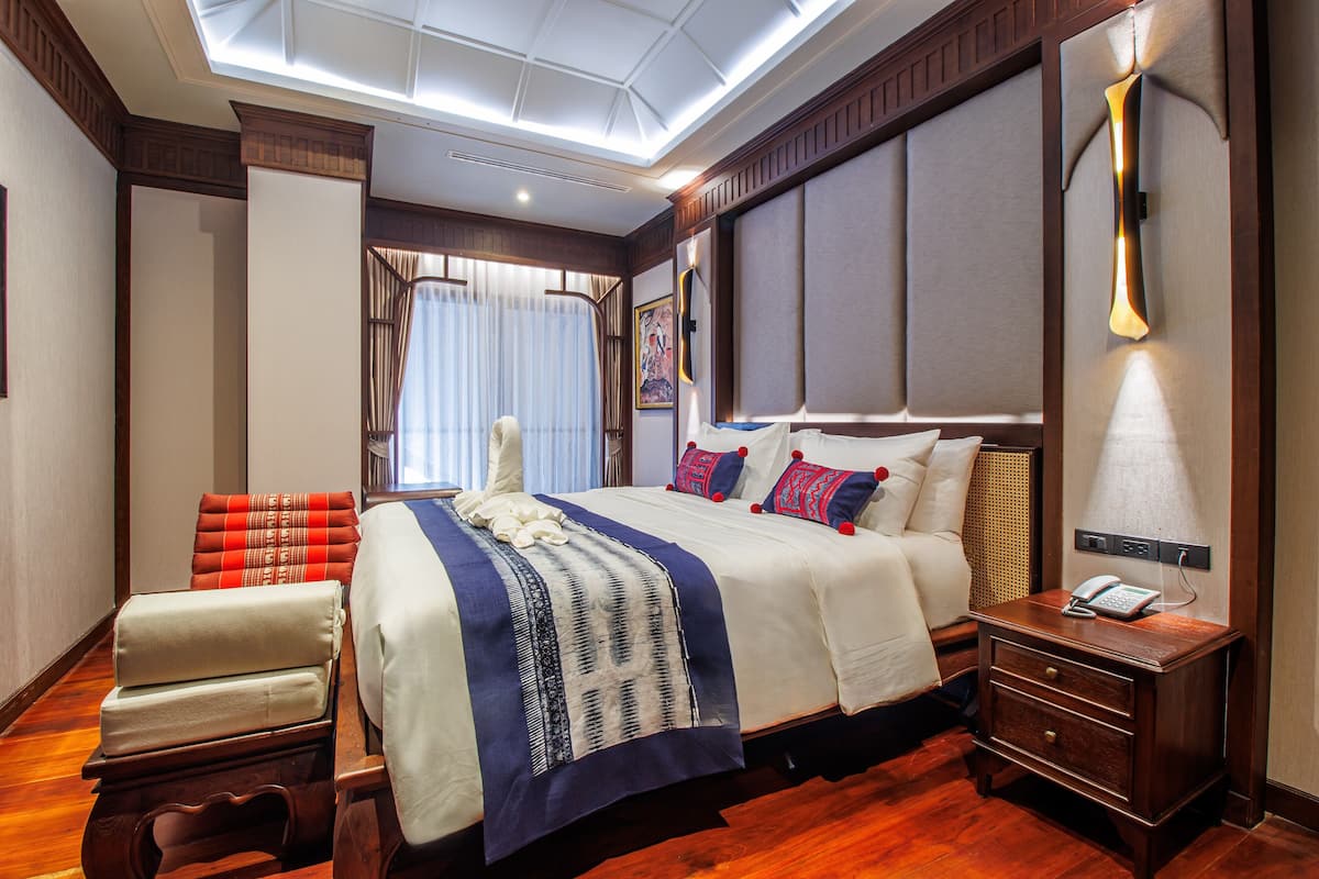 Une chambre d’hôtel avec un grand lit, une table de chevet avec une lampe, une chaise et une fenêtre avec des rideaux.