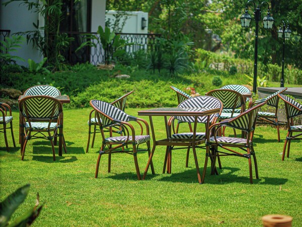 Outdoor seating with wicker chairs and tables, surrounded by lush greenery and a fence. - S48 River Ping Hotel (Chiang Mai)