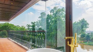 A modern bathroom with a freestanding bathtub, a glass-enclosed balcony with a metal railing, and a view of a river and greenery. - S48 River Ping Hotel (Chiang Mai)