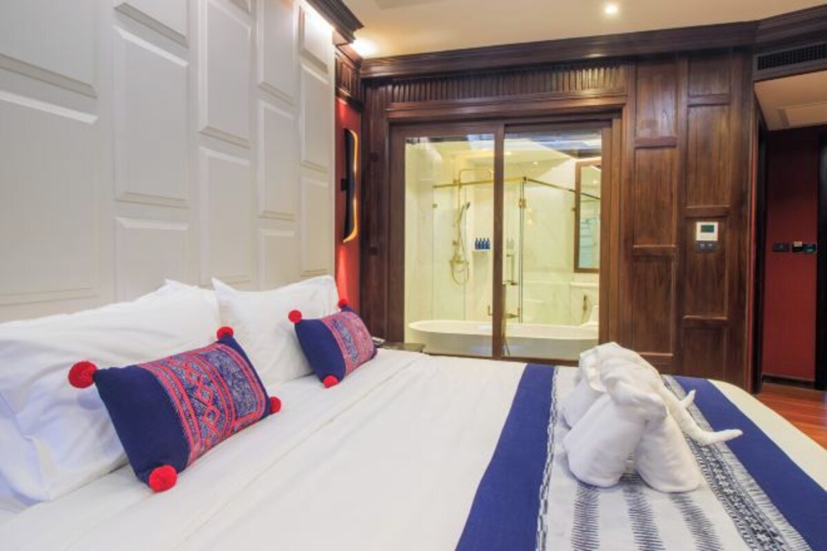 Une chambre d’hôtel avec un grand lit, une salle de bain dotée d’une douche à parois de verre et une porte en bois.