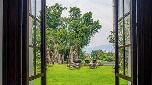 A view through open glass doors of a well-maintained lawn with outdoor furniture, surrounded by trees and a distant mountain range. - S48 River Ping Hotel (Chiang Mai)