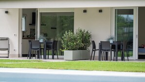 A modern outdoor dining area with a pool, a potted plant, and a sliding glass door leading to a kitchen. - Armonia Suites - Aria -Relax & Nature Just Minutes from Verona (Verona)
