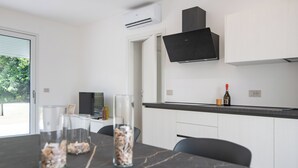 A modern kitchen with white cabinetry, a black countertop, and a wall-mounted TV. There are two glass vases with dried flowers on the table. - Armonia Suites - Aria -Relax & Nature Just Minutes from Verona (Verona)
