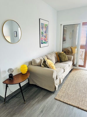 Un salon moderne avec un canapé, un miroir rond, un tableau abstrait encadré et une petite table sur laquelle est posé un vase jaune.