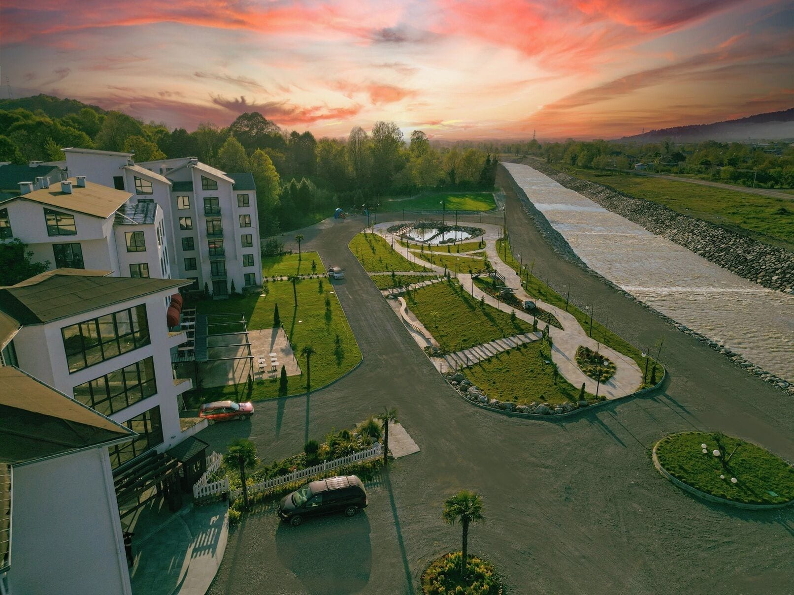 A modern building complex with multiple floors, a central courtyard with a circular water feature, and a surrounding road.