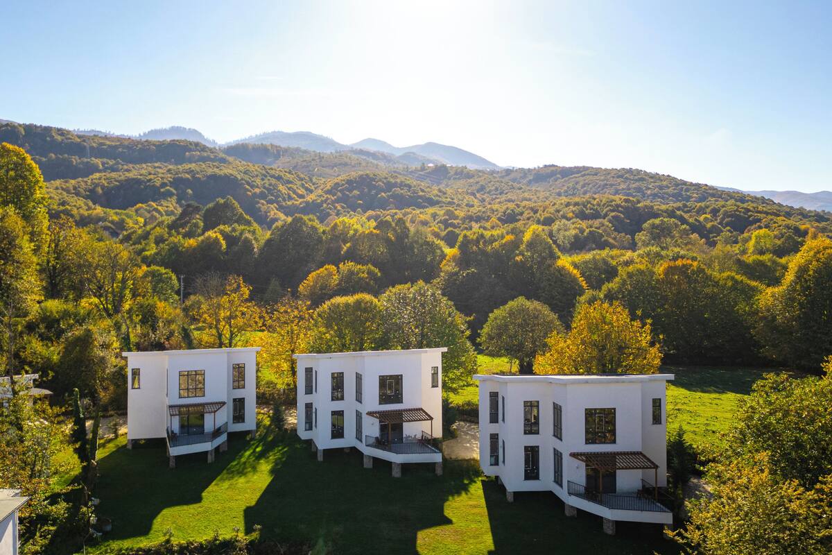 A modern white house with a spacious patio and a view of a lush green valley and mountains.