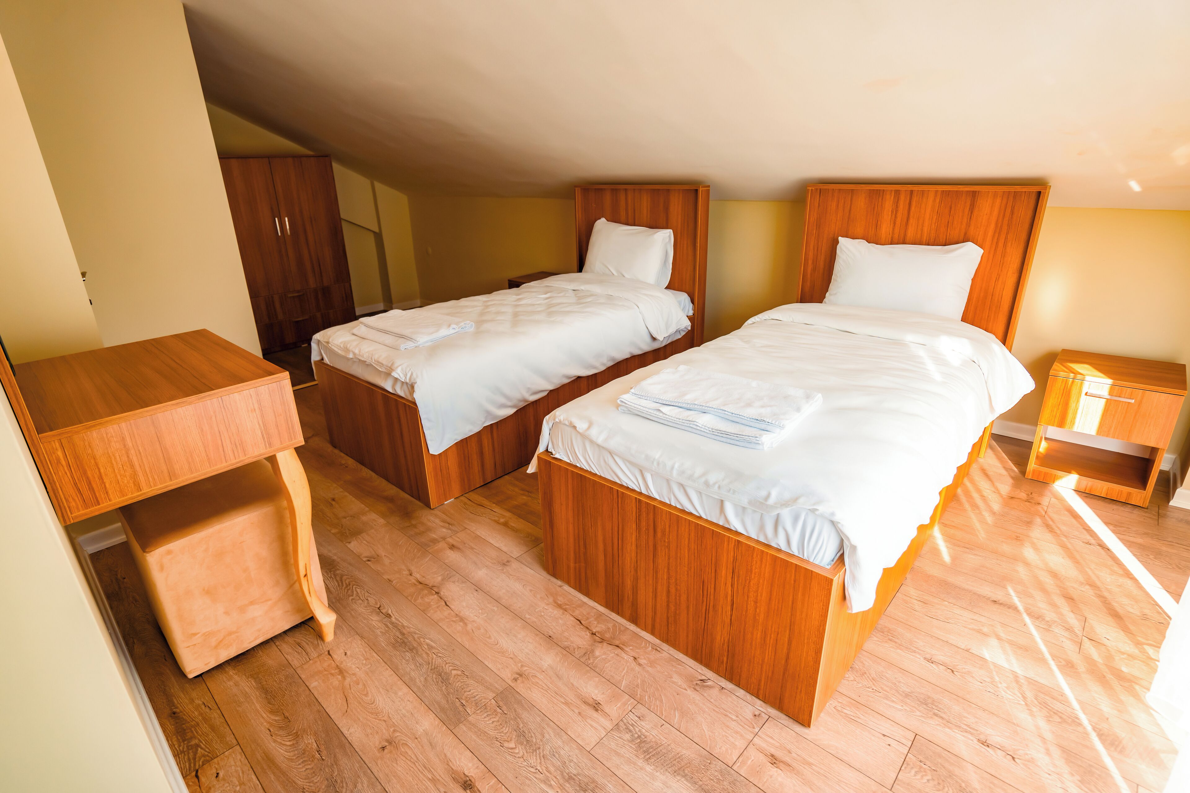 A room with two wooden beds, a wooden desk, and a wardrobe.