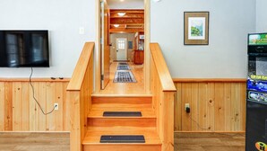 A wooden staircase leading to a second floor with a flat-screen TV mounted on the wall and a gaming console on the right.