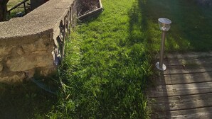 A grassy outdoor area with a stone wall, wooden fence, and a solar-powered light post. - Champsaur : Authentic gîte 1250m - Exceptional mountain view - Garden (Saint-Bonnet-en-Champsaur)