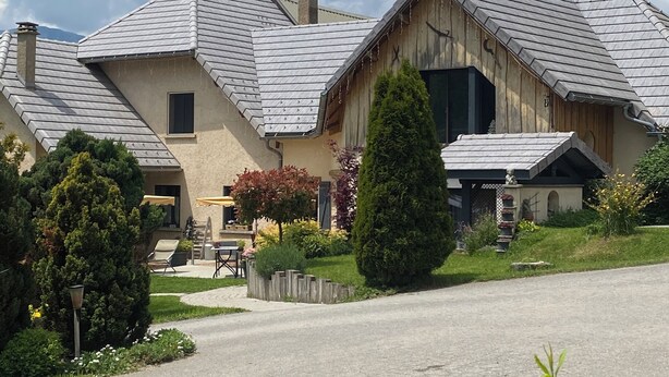 A large, two-story house with a sloped roof, a chimney, and a well-maintained garden with various plants and a patio area. - Champsaur : Authentic gîte 1250m - Exceptional mountain view - Garden (Saint-Bonnet-en-Champsaur)