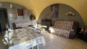 A dining area with a table and chairs, a sofa, and a tiled floor. - Champsaur : Authentic gîte 1250m - Exceptional mountain view - Garden (Saint-Bonnet-en-Champsaur)
