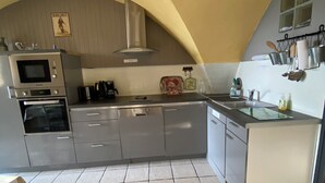 A compact kitchen with a microwave, oven, and dishwasher, featuring a tiled floor and a curved ceiling. - Champsaur : Authentic gîte 1250m - Exceptional mountain view - Garden (Saint-Bonnet-en-Champsaur)