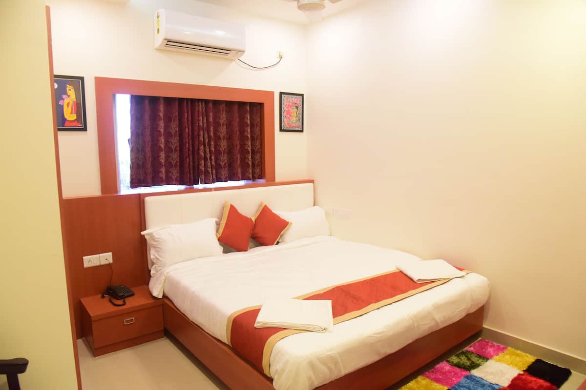 A neatly made bed with a red and white bedspread, a bedside table with a phone, and a window with curtains.