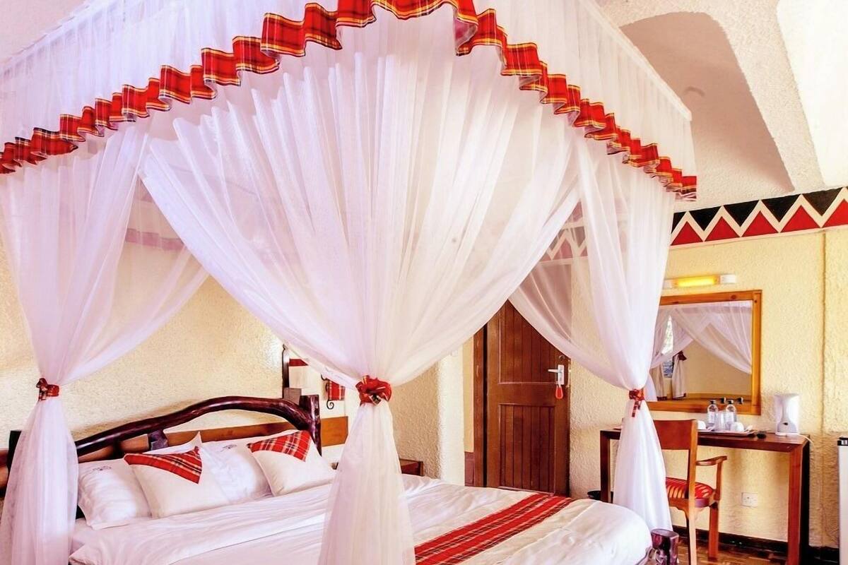 A bed with a canopy, a wooden floor, a desk, and a mirror.