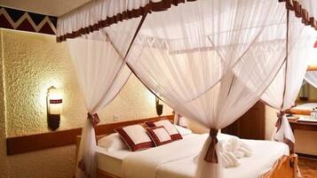 A four-poster canopy bed with white linens and brown pillows in a room with textured walls and a wooden floor.