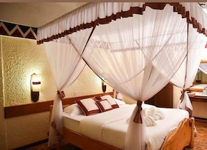 A four-poster canopy bed with white linens and brown pillows in a room with textured walls and a wooden floor. - Maasai Lodge (Nairobi)