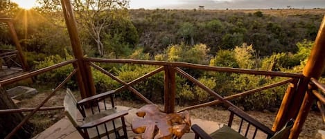 Um deck de madeira com mesa e cadeiras com vista para uma paisagem natural.