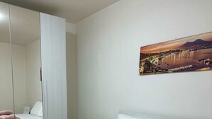 A bedroom with a bed, a nightstand, a mirror, and a wall-mounted picture.
