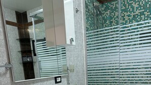 A modern bathroom with a white sink, a glass shower enclosure, and a built-in washing machine.
