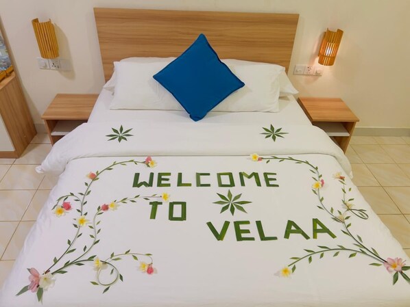 A bed with a white bedspread featuring floral designs and the text "WELCOME TO VELAA". - Moro Fohdhoo (Fodhdhoo)