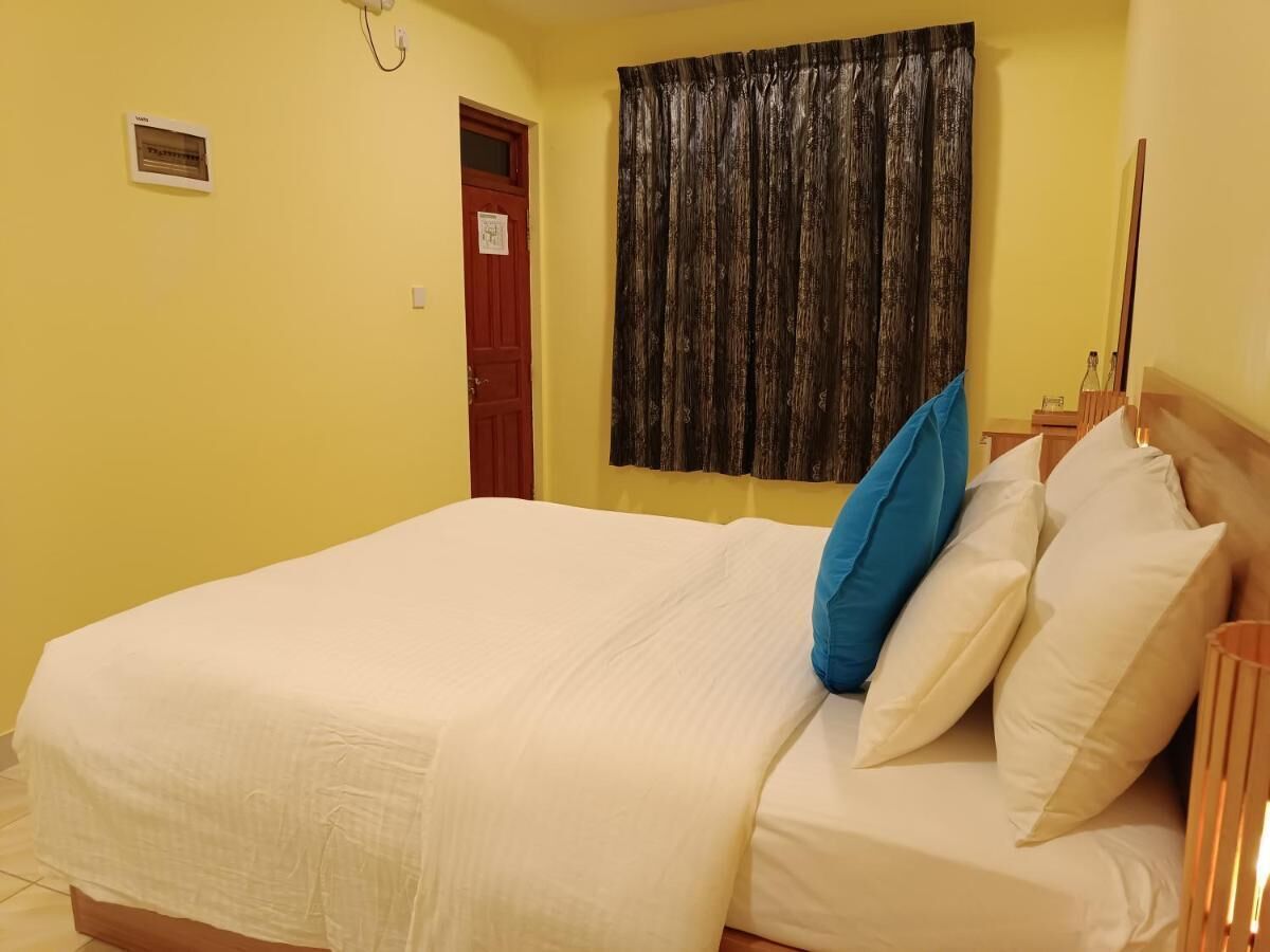 A bedroom with a bed, a door, a curtain, and a nightstand with a lamp.