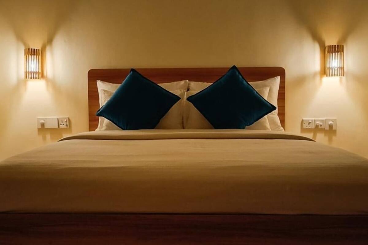 A neatly made bed with a wooden headboard, two wall-mounted light fixtures, and a power outlet on each side of the bed.