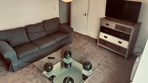 Una sala de estar con un sofá gris, una mesa de centro de cristal con tres objetos esféricos, un televisor sobre un mueble bajo y un aparador gris con cajones.