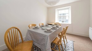 Un comedor con una mesa lista para cuatro personas, sillas de madera, un mantel estampado y una ventana con vistas.