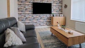 A modern living room with a stone-patterned wall, a mounted TV, a wooden cabinet, and a leather sofa. - Cedar Drive (Weymouth)