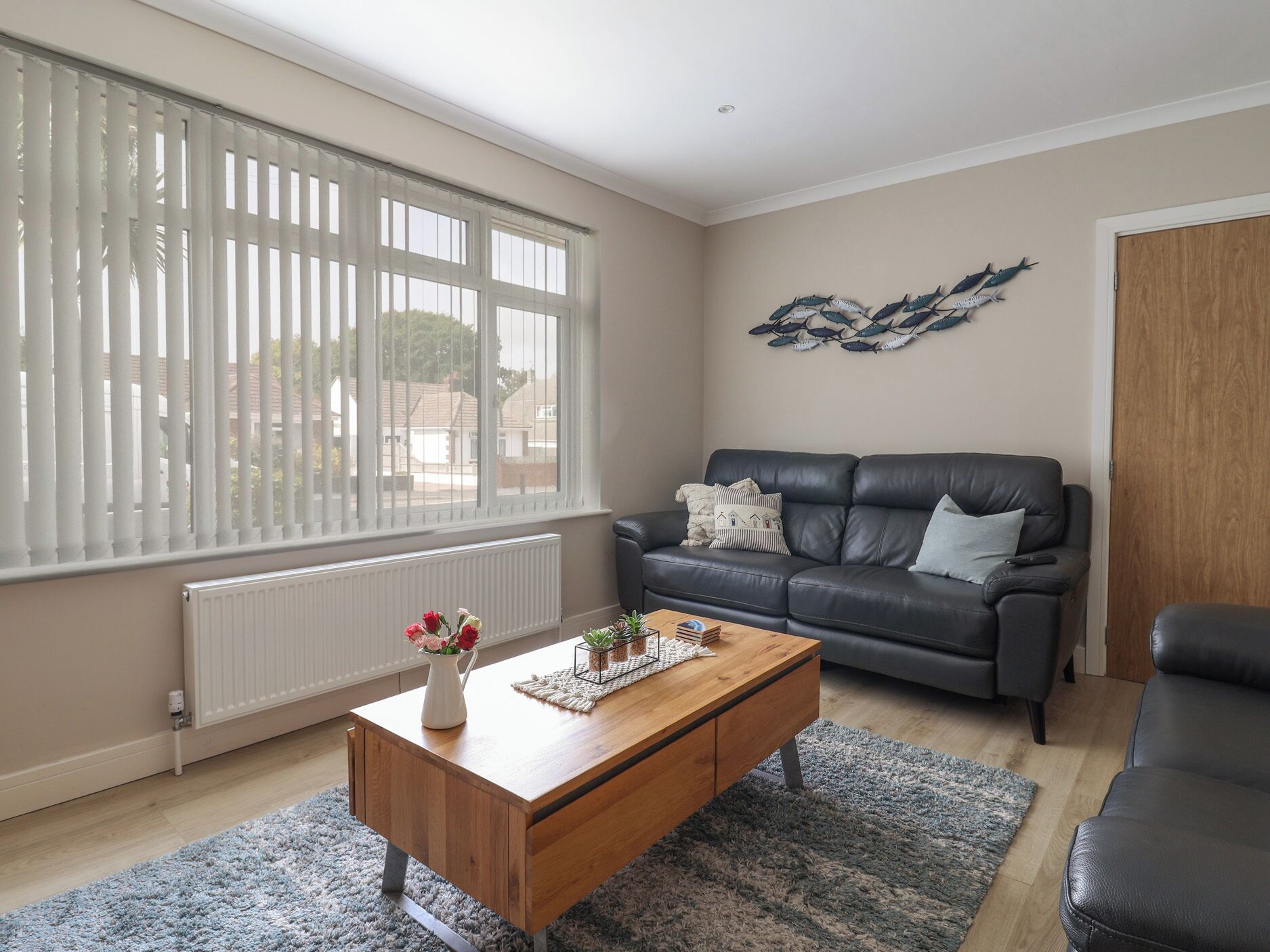 A living room with a dark leather sofa, a wooden coffee table, and a large window with blinds.