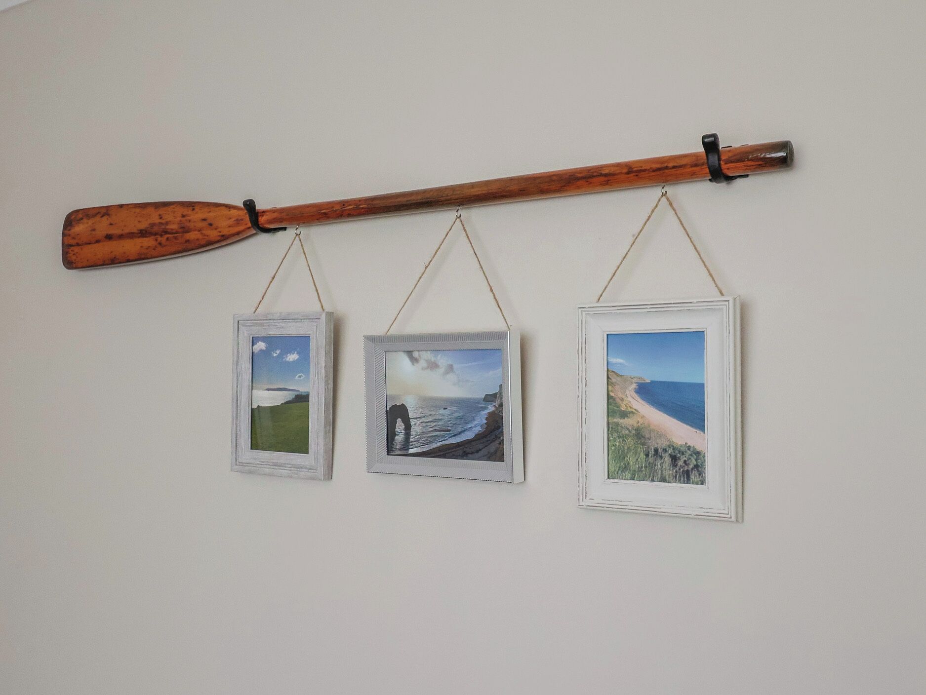Tre inramade bilder hänger på en vägg, och ovanför dem finns en träpaddel.